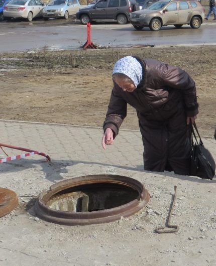 An elderly woman looks into a sewer well