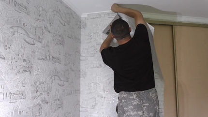 A man is covering the walls with non-woven wallpaper